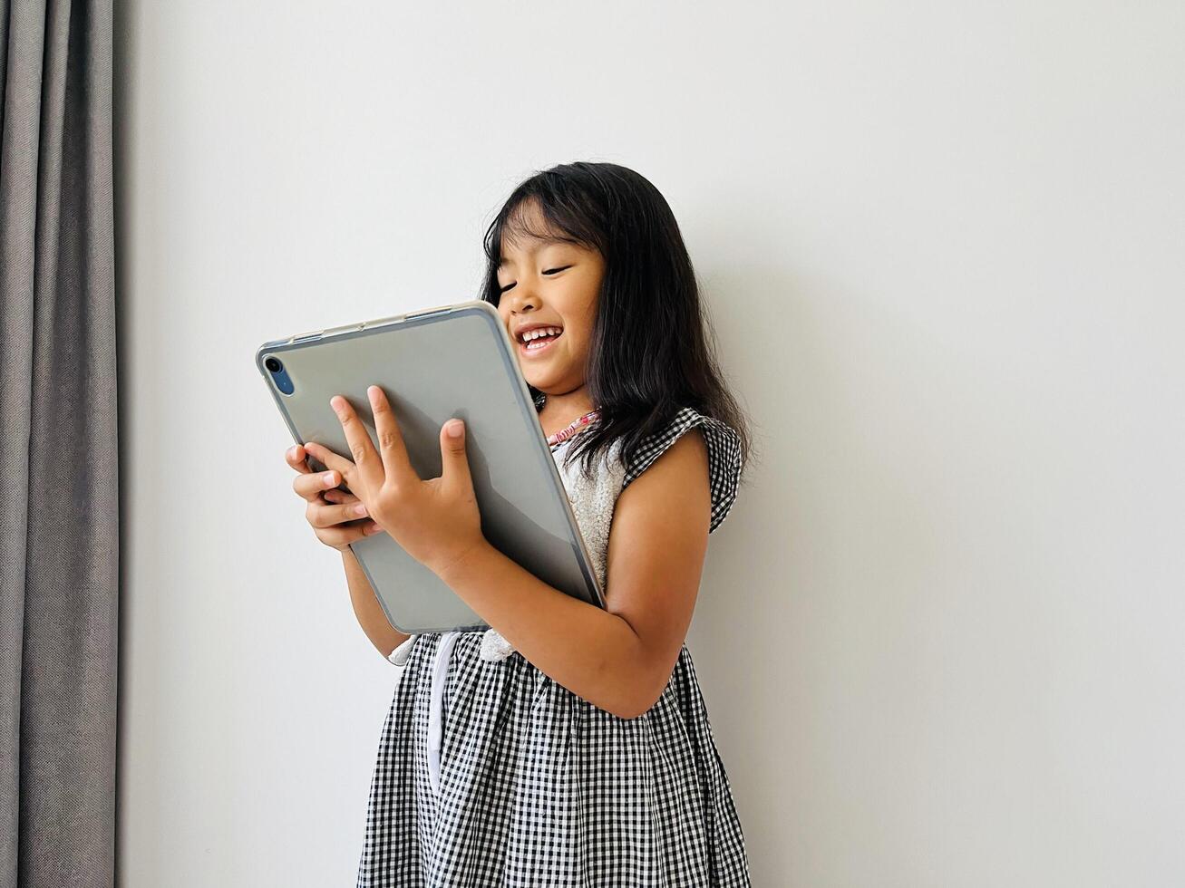 Happy adorable five year old girl playing online learning game on mobile tablet. Watching cartoons on mobile tablet. Asian little girl watching tablet laying on the bed at home. Addicted to gadget. photo