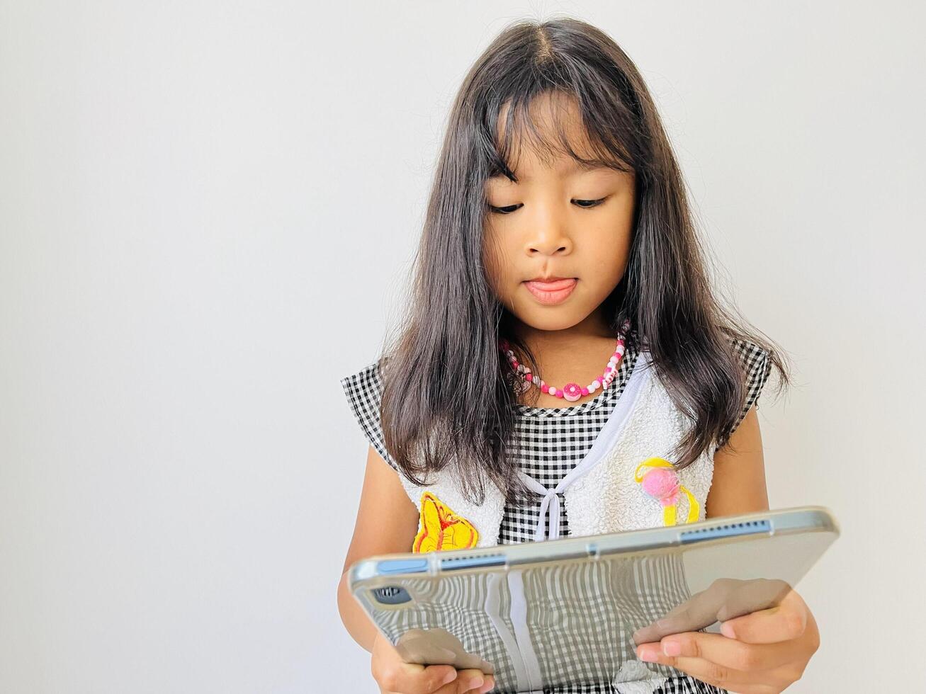 Happy adorable five year old girl playing online learning game on tablet. Watching cartoons on mobile tablet. Asian little girl watching tablet at home. Addicted to gadget. photo