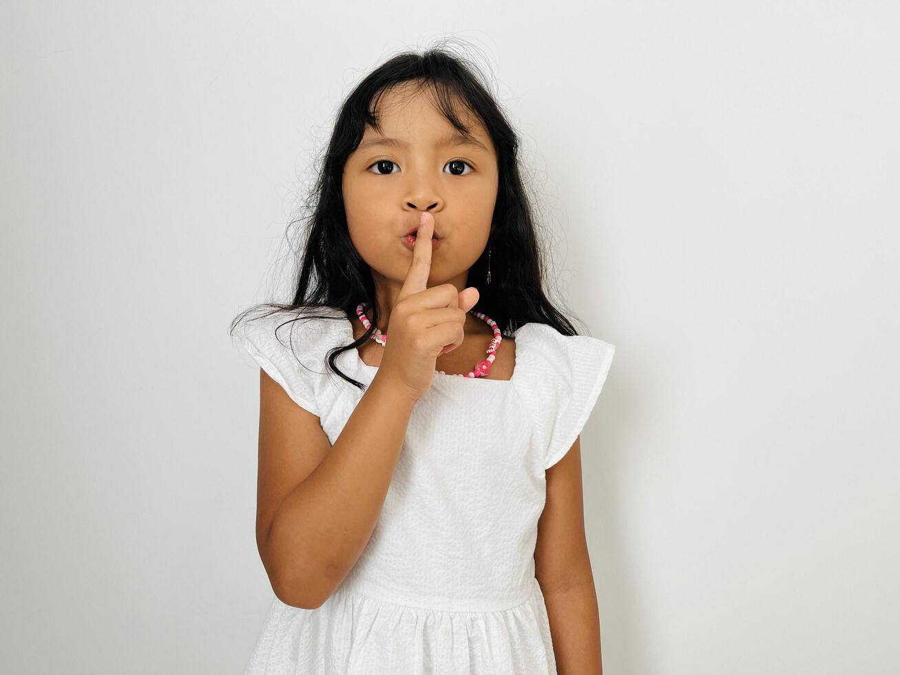 Emotional child girl has secret. Little girl with wonder face keeps finger on lips, shows silence sign, asks to be quiet and stop make loud noise. Silent gesture. photo