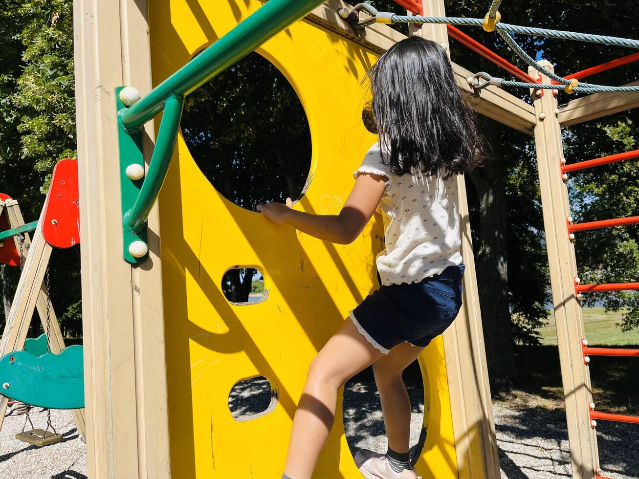 Cute Asian preschooler girl having fun on outdoor playground. Spring summer autumn active sport leisure for child. Activity for family with children. Equipment of entertainment park for kids. photo