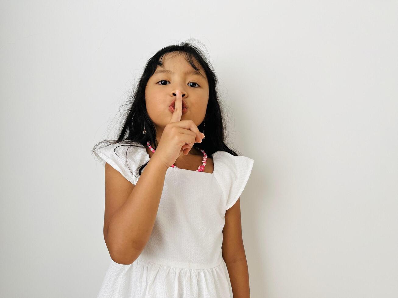 Emotional child girl has secret. Little girl with wonder face keeps finger on lips, shows silence sign, asks to be quiet and stop make loud noise. Silent gesture. photo