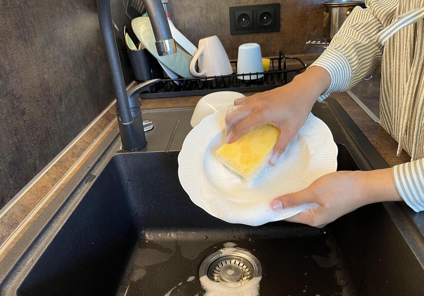 Close up of woman housewife is doing the dishes at home kitchen by using wash sponge and dishwashing soap. Clean the plate photo