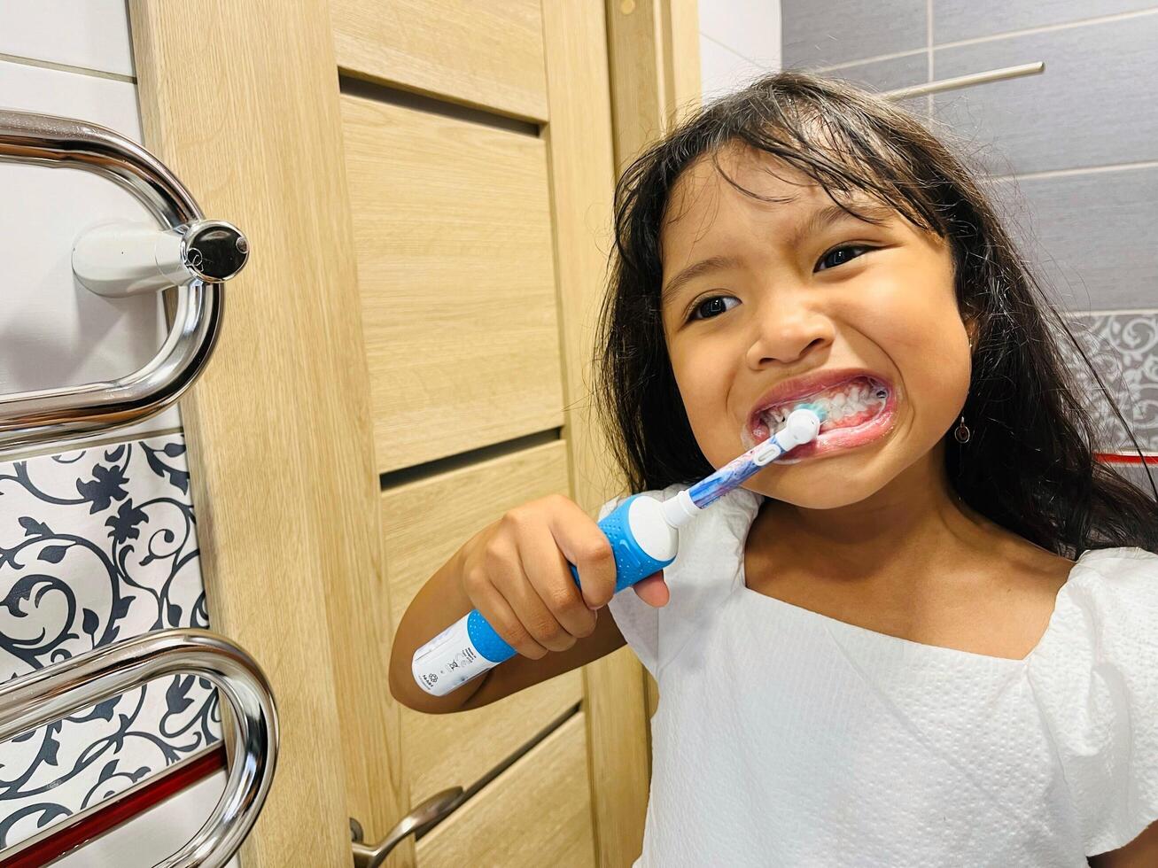 A happy little Asian girl brushes her teeth in the bathroom. Morning routine. Hygiene. Healthy lifestyle photo