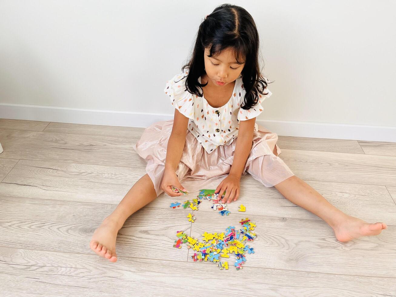 A five year old Asian girl is sitting on the floor with a wooden motif playing with jigsaw puzzle photo