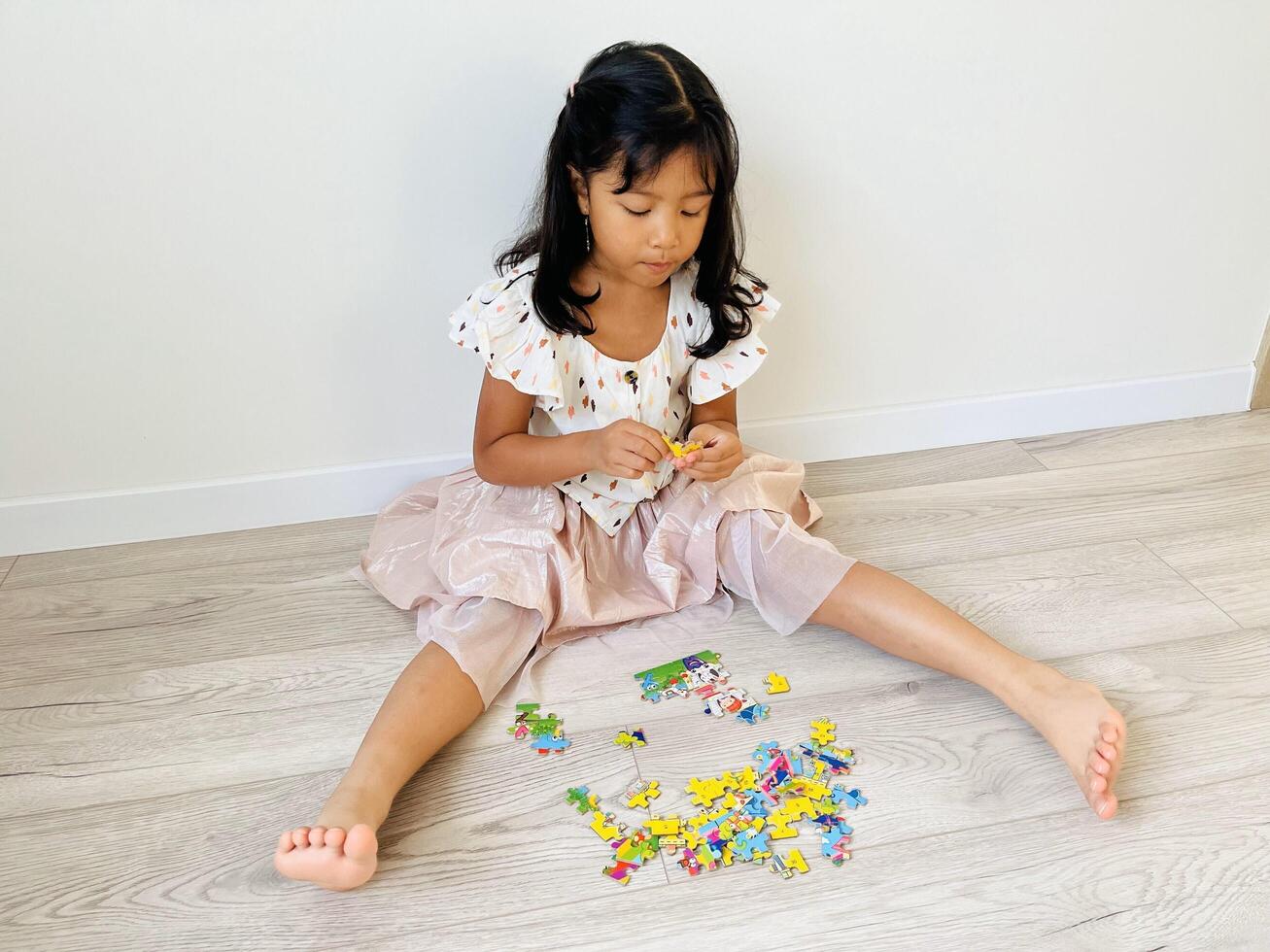 A five year old Asian girl is sitting on the floor with a wooden motif playing with jigsaw puzzle photo