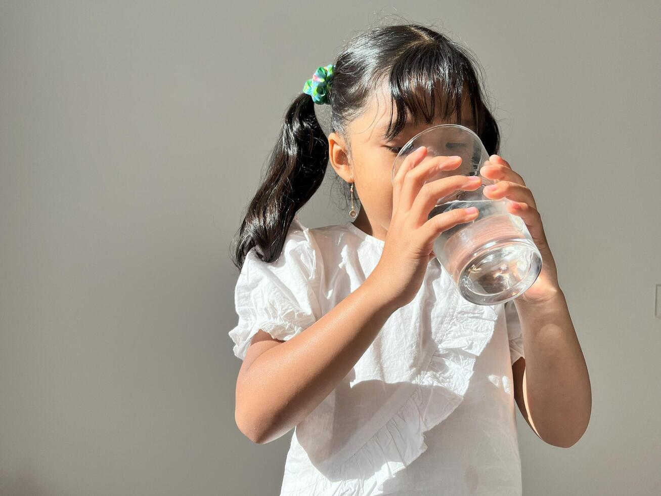 An Asian girl is drinking A glass of pure clean mineral water, recommending healthy lifestyle, everyday. Stop drinking aerated water or soft drink, water are great for kid. photo