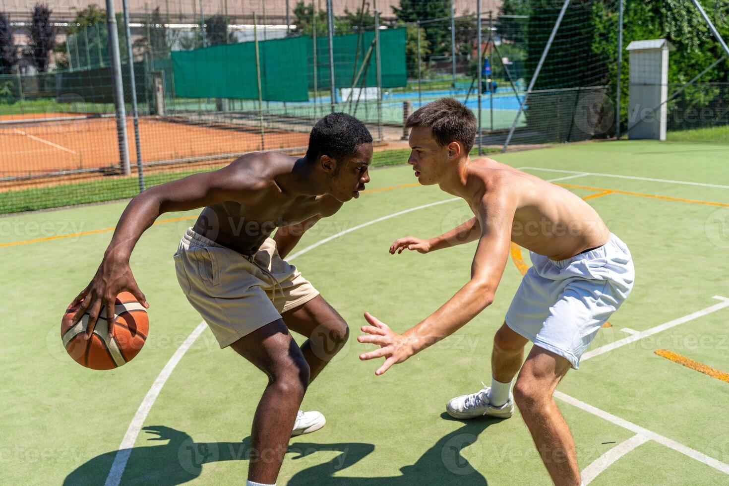 two young multi-ethnic athletes basketball players in action face each other on the artificial grass playing field on a sunny summer day photo