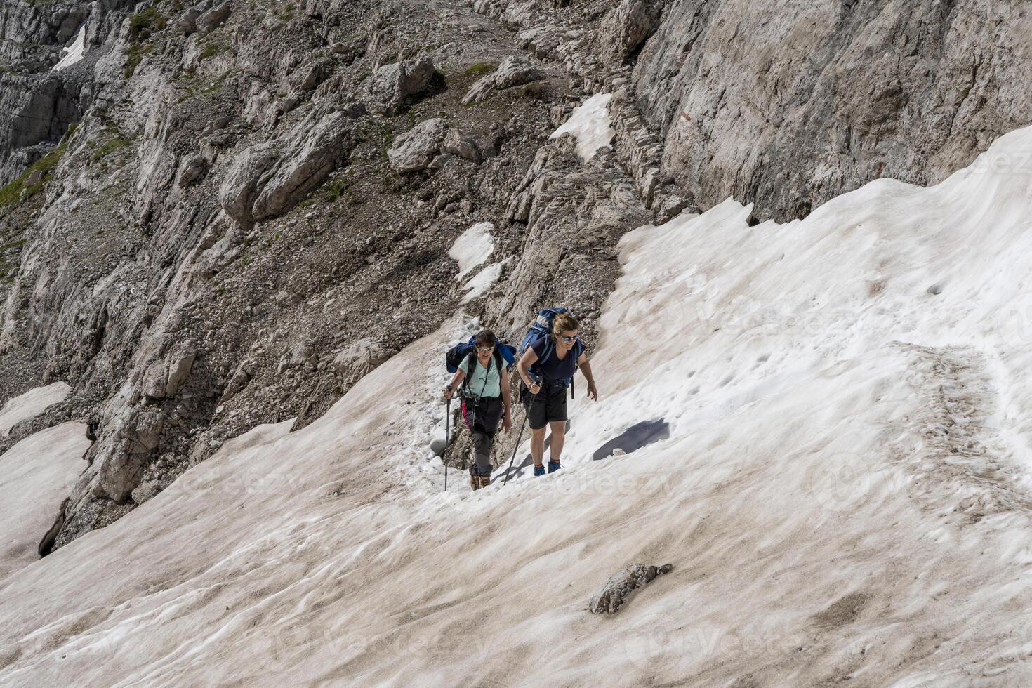 two experienced female hikers are climbing a snowy valley in the Dolomites photo