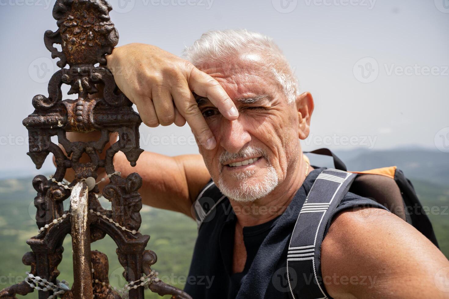 smiling mature man taking a selfie on top of a mountain dressed in sports clothes photo