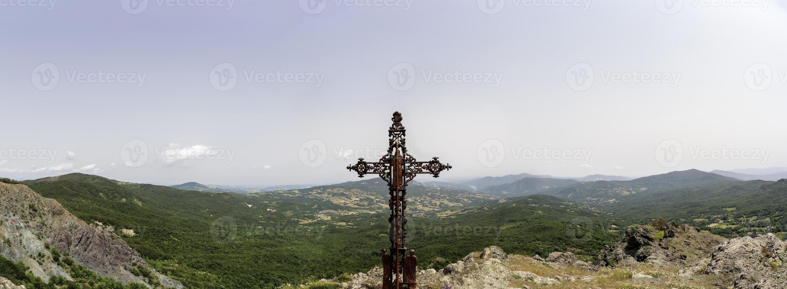 closeup of a rusty metal cross in front of a landscape of the hills photo