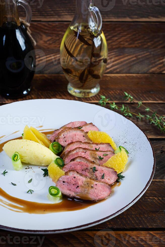 Roast duck fillet with mashed potato and orange sauce on wooden background photo