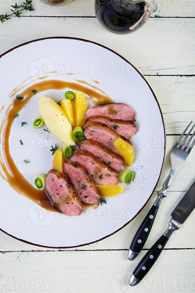 Roast duck fillet with mashed potato and orange sauce on wooden background photo