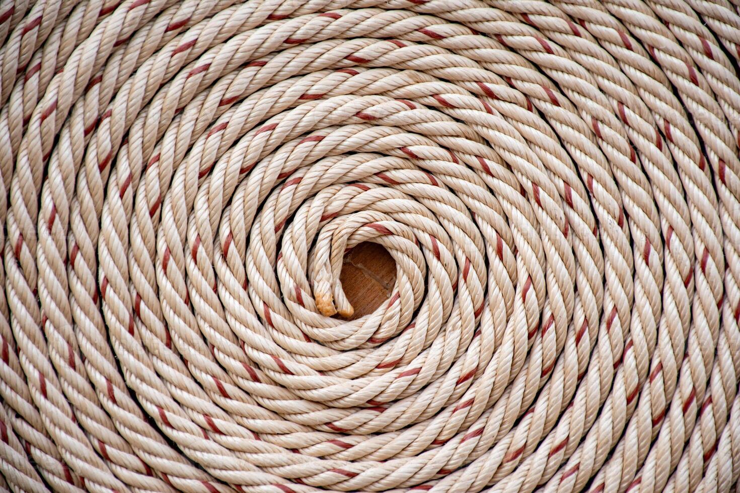 White rope with red lines and coiled roll from top view on wooden table background in warm tone. Braided rope on a roll background texture 2025. Photo of an old vintage rope.