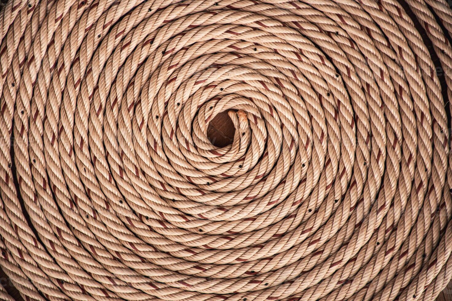 Brown rope with red lines and coiled roll from top view on wooden table background in warm tone. Braided rope on a roll background texture 2025. Photo of an old vintage rope.