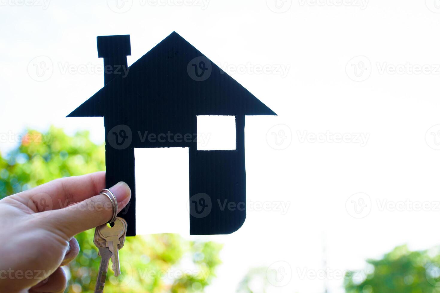 Man hand holding small icon house model and keys against nature and sky sunset background. hands holding symbol paper of building for concept of dream to buy house family and real estate 2025. photo