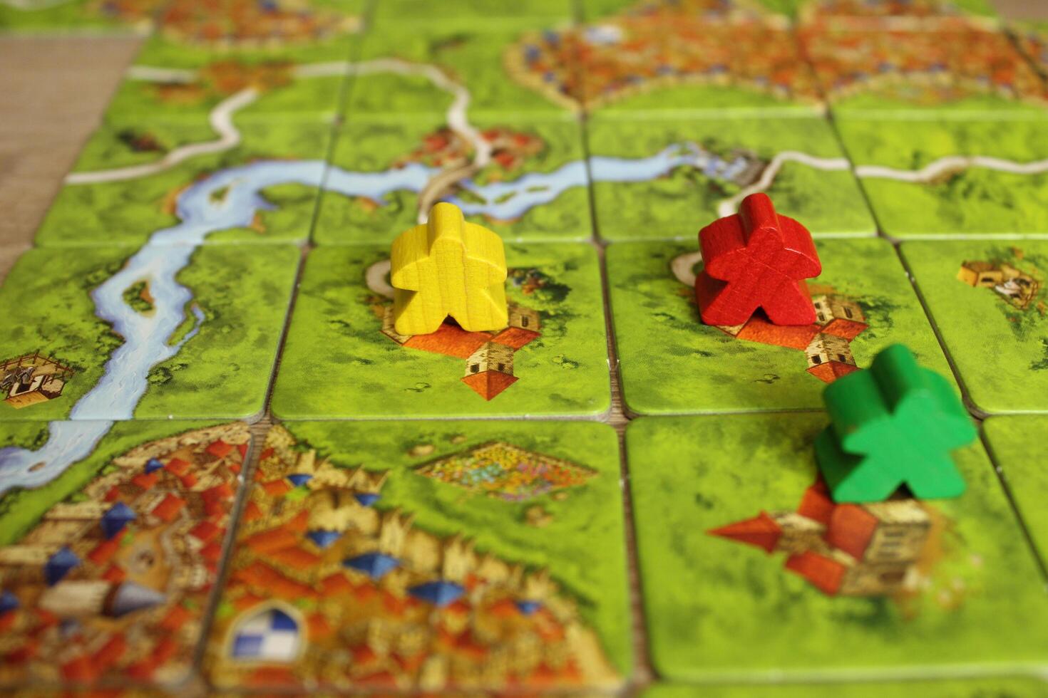 board family game carcassonne green yellow red meeple on the map tiles of the playing field. Rules for placing monasteries on carriages photo