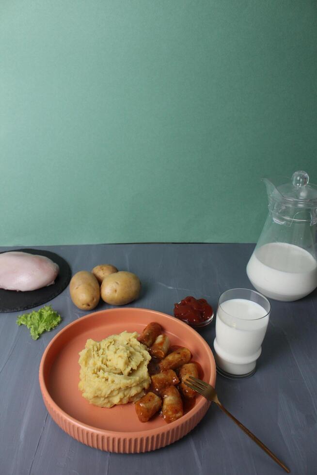 Serving lunch, potatoes with sausages, a glass of milk and ingredients for cooking, potatoes, chicken breast, milk on a gray background, space for copyspace text photo
