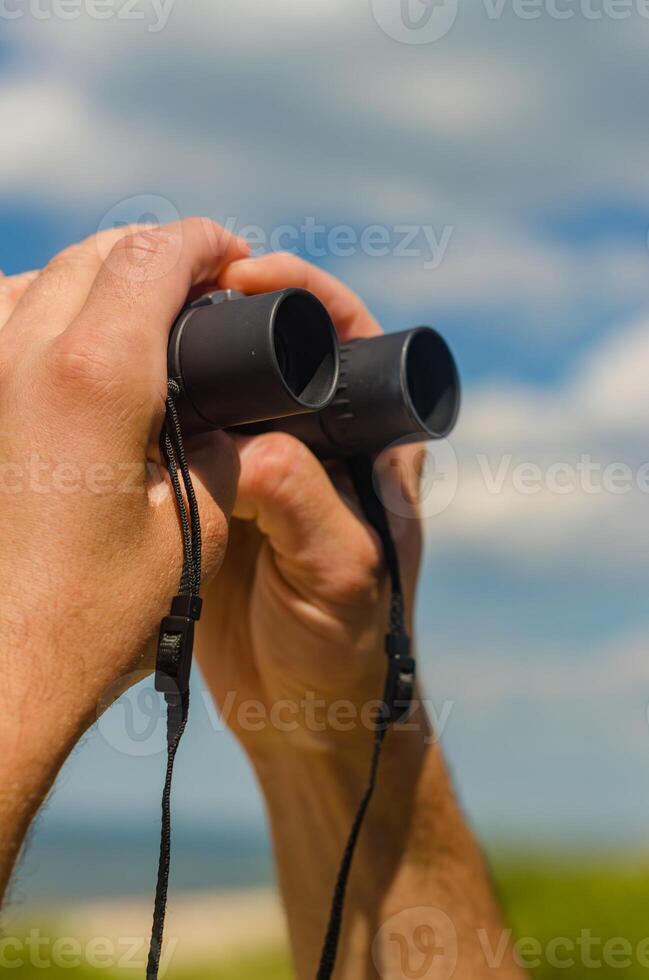 Male hand are holding binoculars on the beach. High quality photo