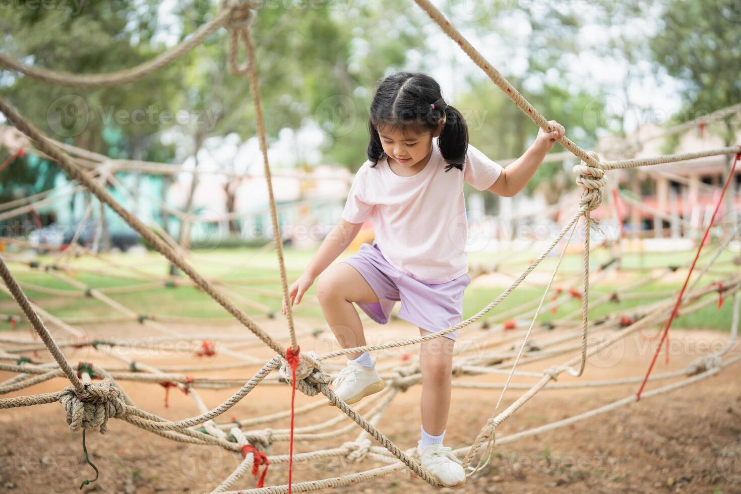 Asian young girl is playing on a rope course, climbing up and down the ropes. The scene is lively and playful, with the girl enjoying herself as she navigates the course photo