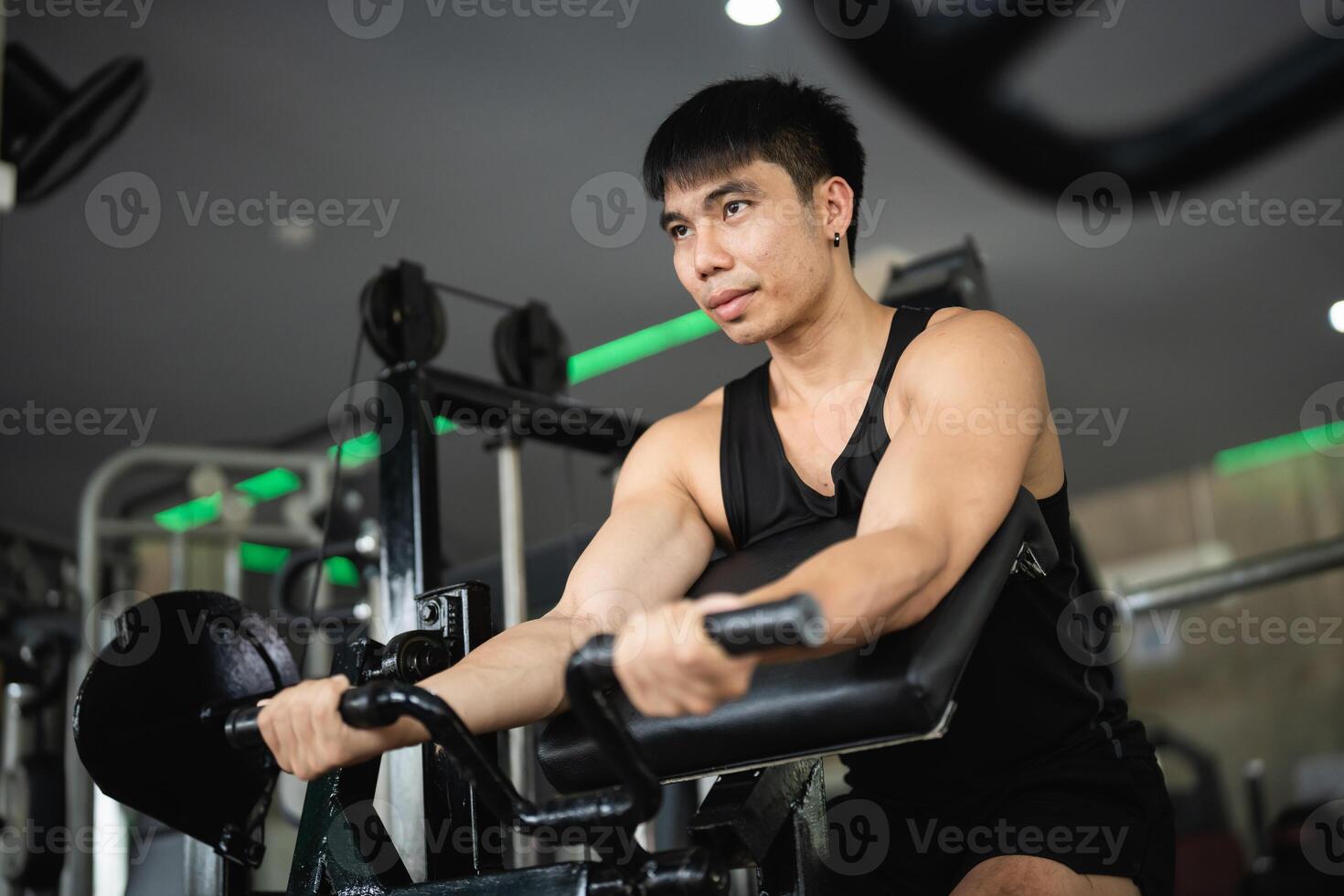 Asian man is working out in a gym, lifting weights and doing pushups. The gym is filled with various exercise equipment, including a bench and a machine. The atmosphere is energetic and focused photo