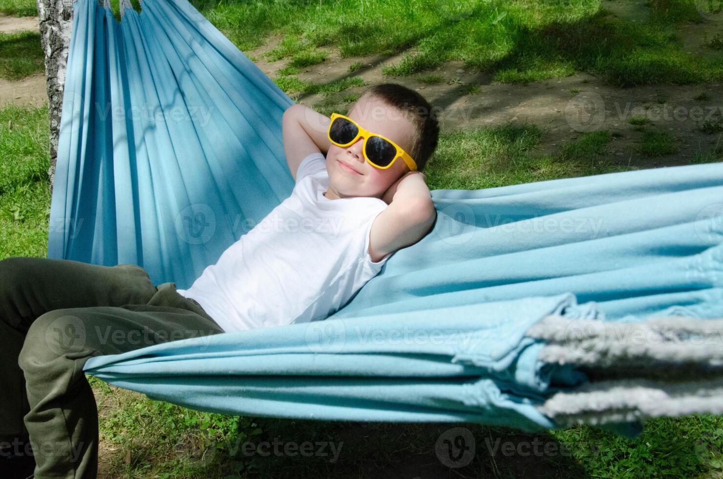 Cute little blond caucasian boy relaxing and having fun in multicolored hammock photo