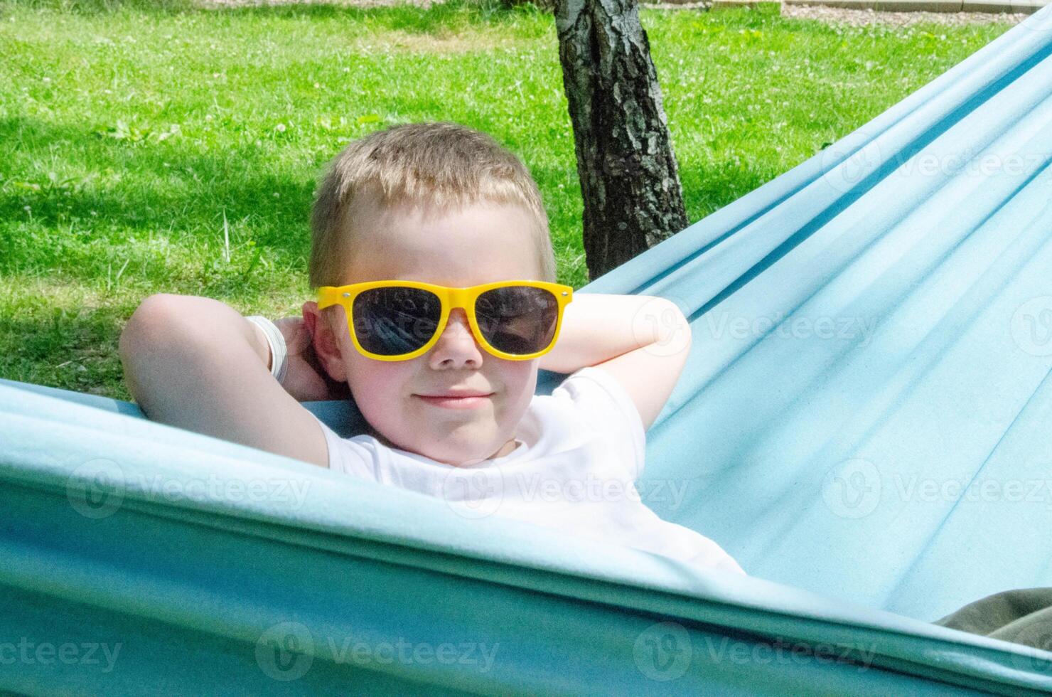 Cute little blond caucasian boy relaxing and having fun in multicolored hammock photo