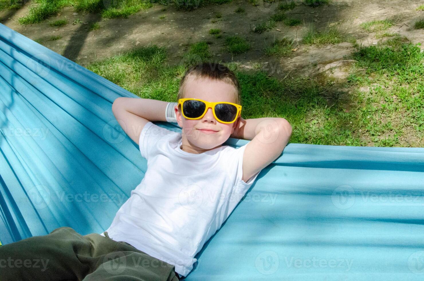 Cute little blond caucasian boy relaxing and having fun in multicolored hammock photo