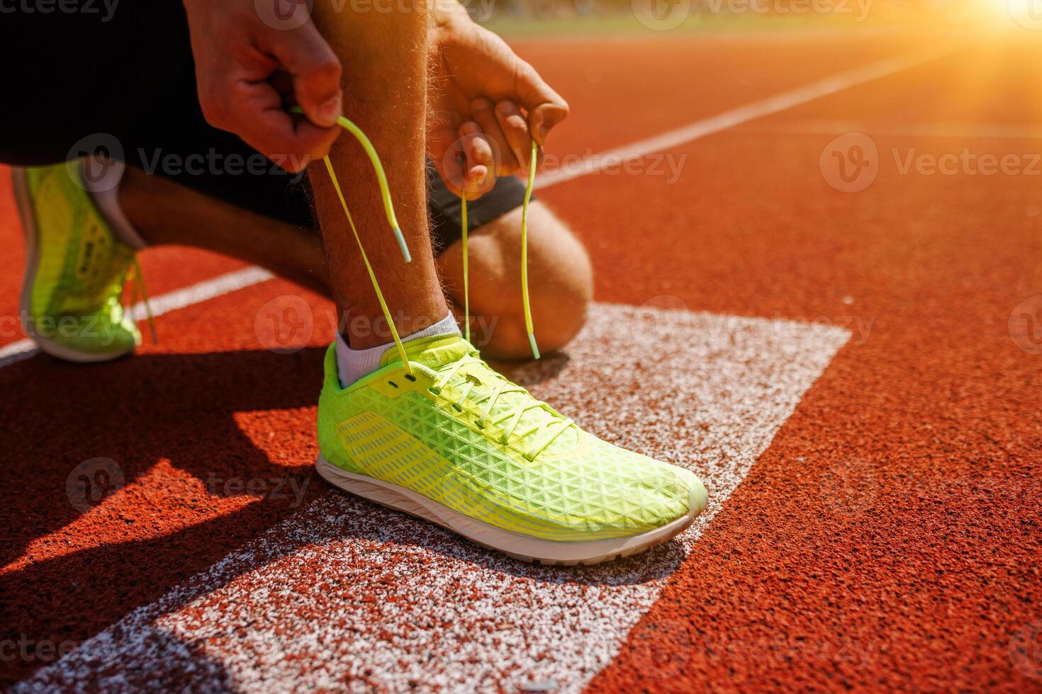 A runner ties neon yellow shoes on the track at sunrise, showing dedication to a healthy lifestyle photo