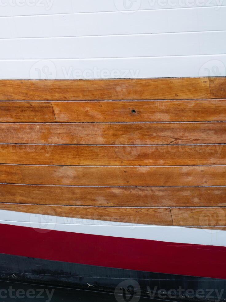 A pattern of stripes in white, red, black, and natural stain on the side of a boat. photo