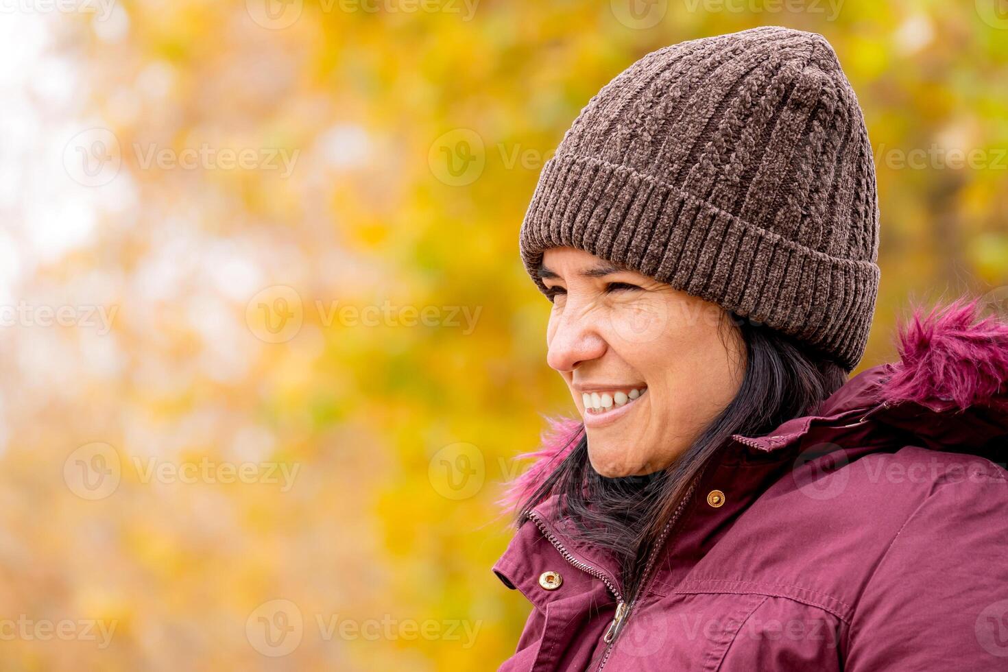 Latin woman with a hat in a natural autumn landscape. It is a smiling semi profile portrait. photo