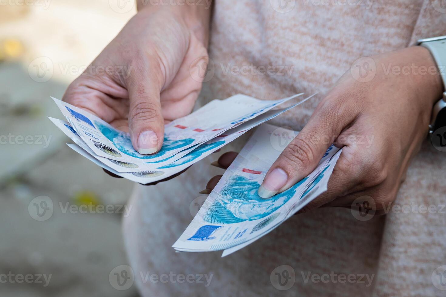 A woman counts ten thousand Argentine peso bills on the street. Close up photo of her hands.