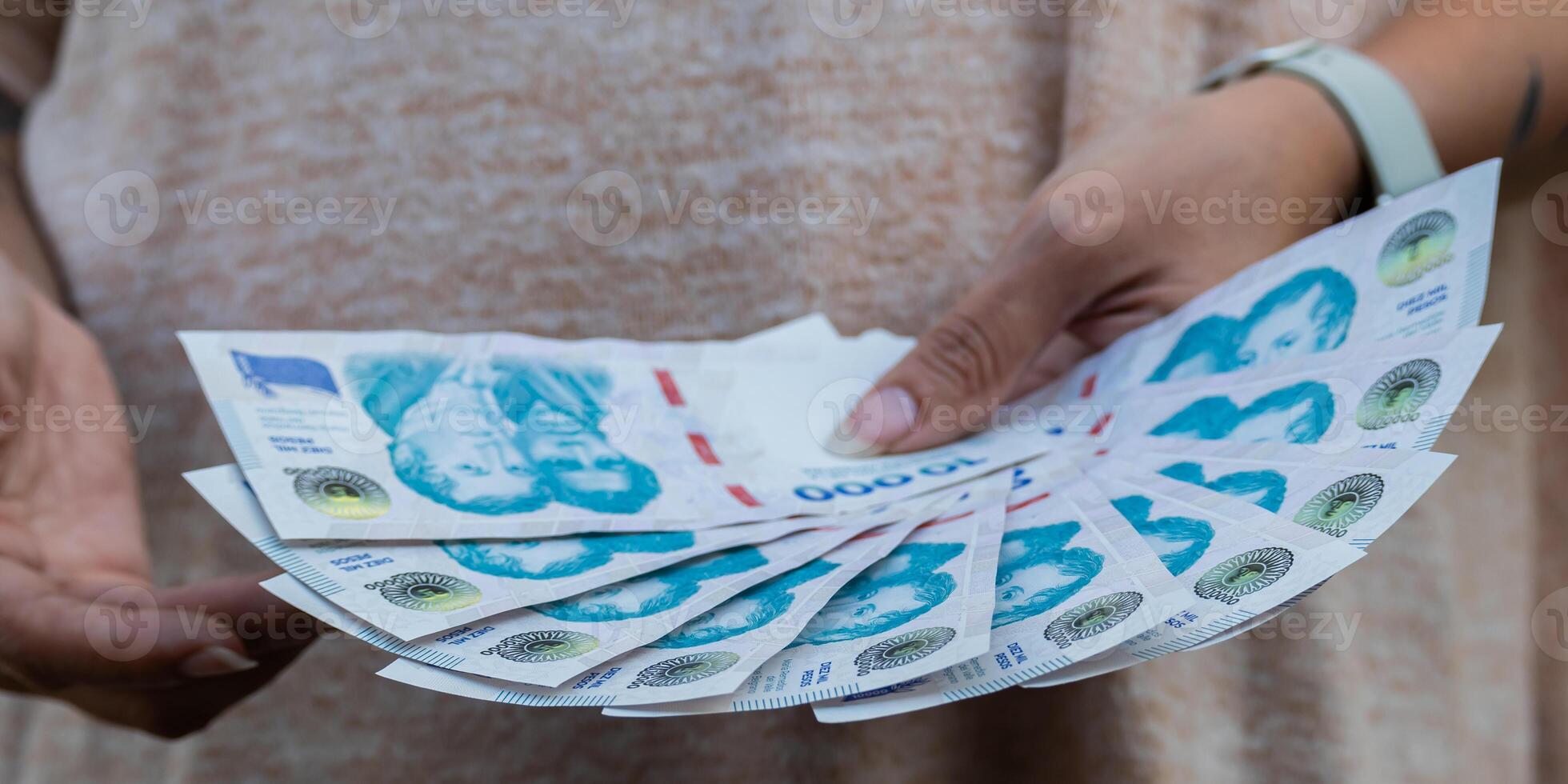 Ten thousand Argentine peso bills 2024. Woman holds 100,000 Argentine pesos in her hands with the new Argentine bills. photo