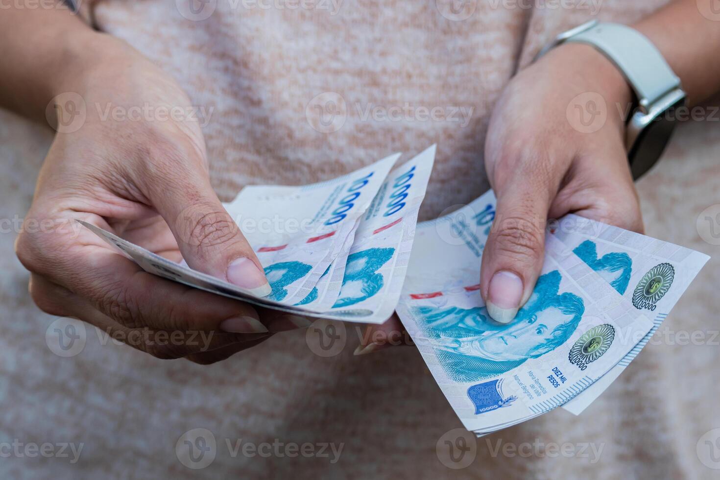 Front photo of a woman's hands counting 10,000 Argentine peso bills.