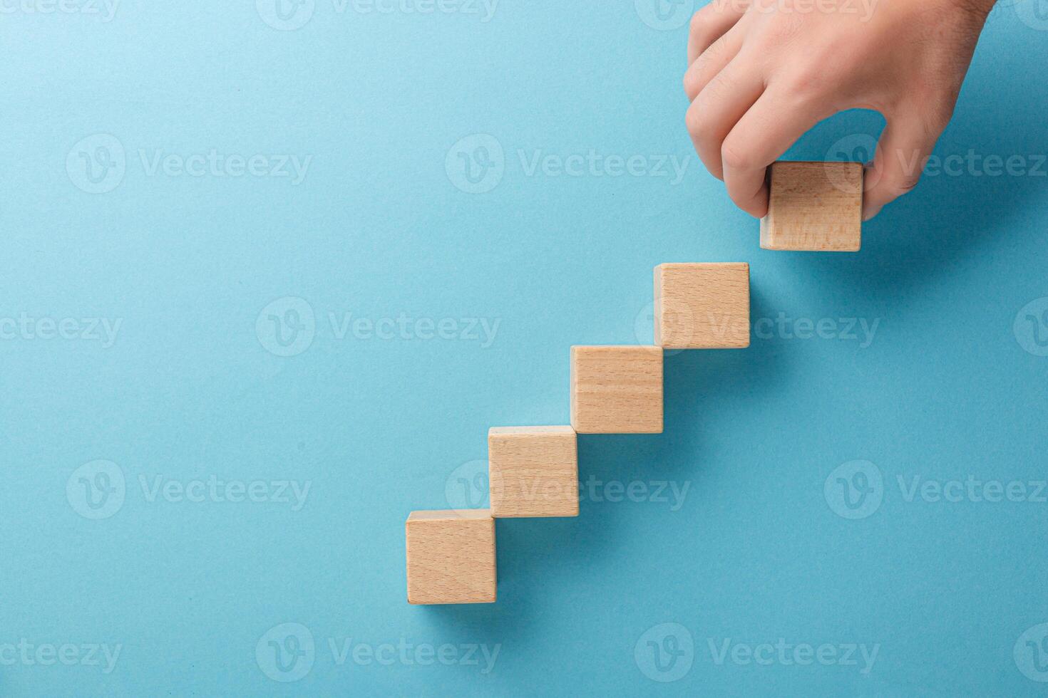 wooden cubes in the form of a ladder with a hand on a blue background photo