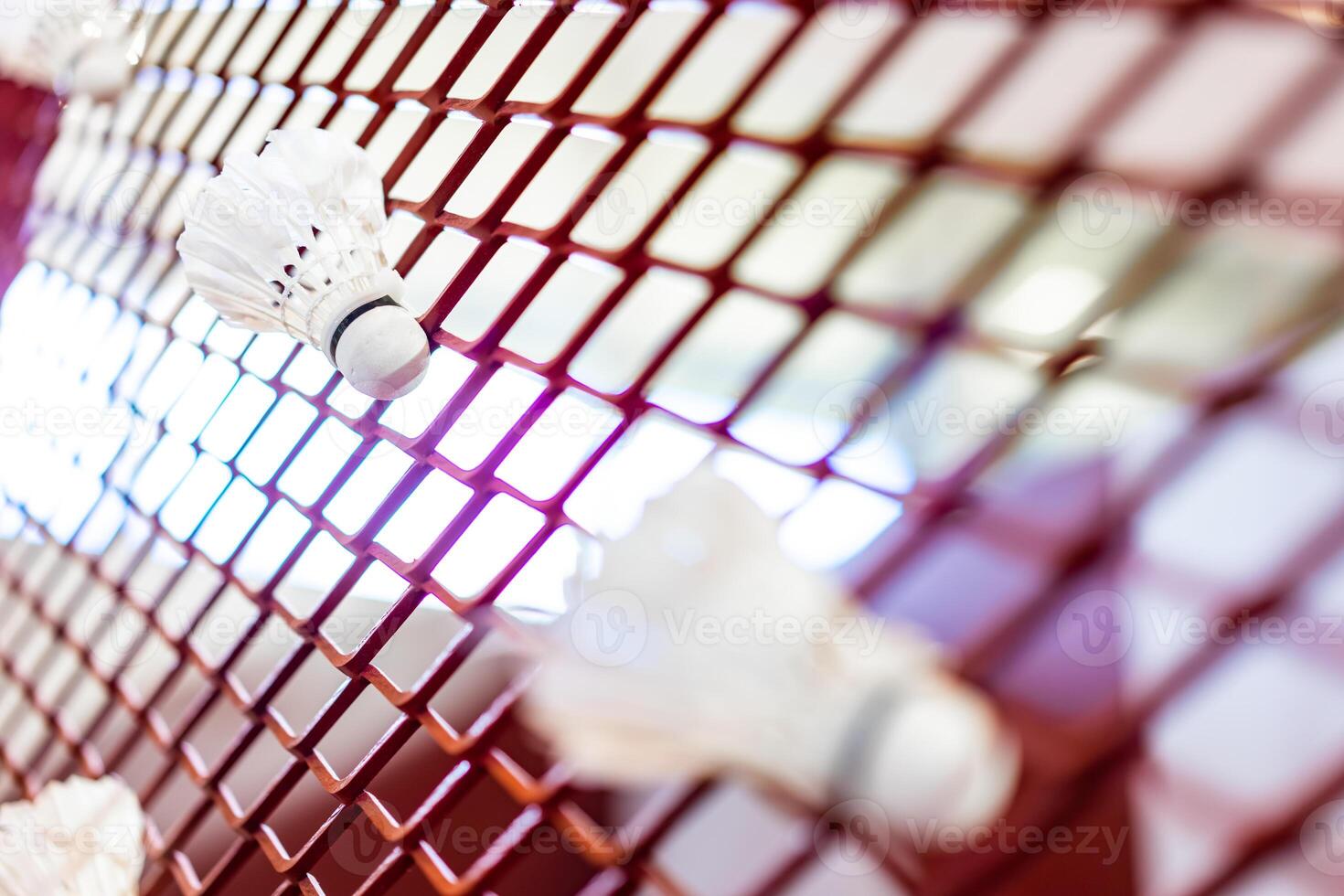 Shuttlecocks were stuck to the badminton steel grill net with a big red drawing of shuttlecock on background beside. photo