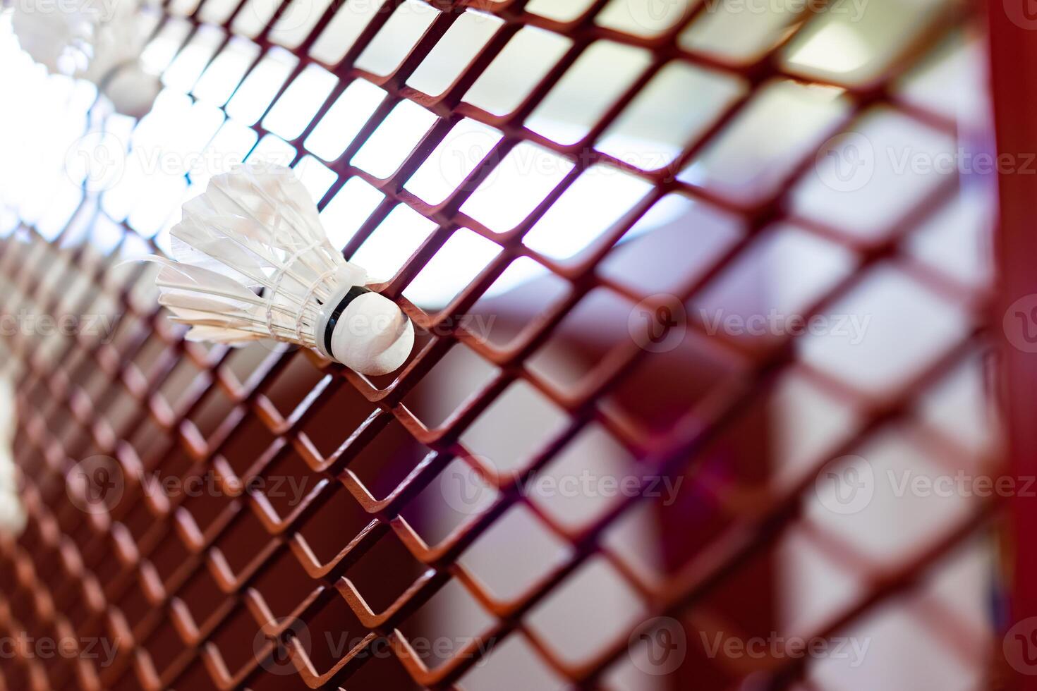 Shuttlecocks were stuck to the badminton steel grill net with a big red drawing of shuttlecock on background beside. photo