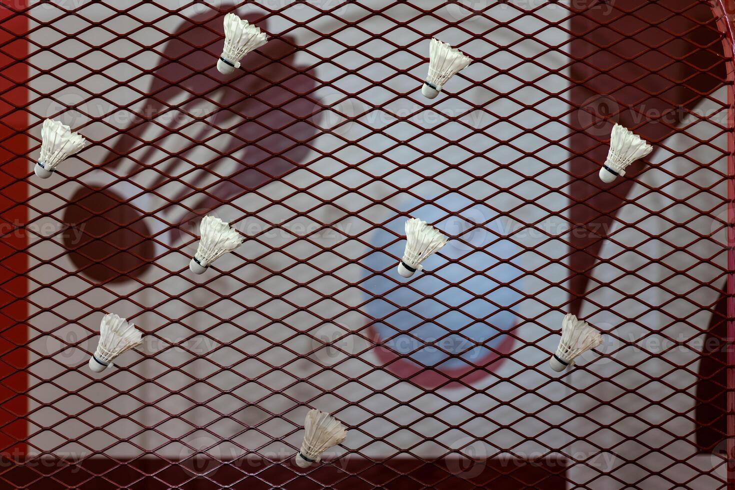 Shuttlecocks were stuck to the badminton steel grill net with a big red drawing of shuttlecock on background beside. photo