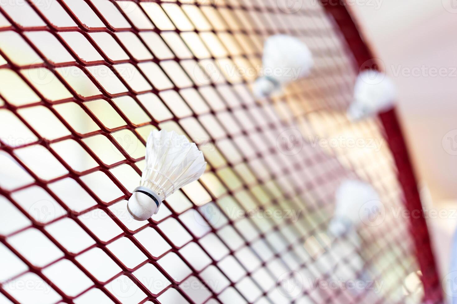 Shuttlecocks were stuck to the badminton steel grill net with a big red drawing of shuttlecock on background beside. photo