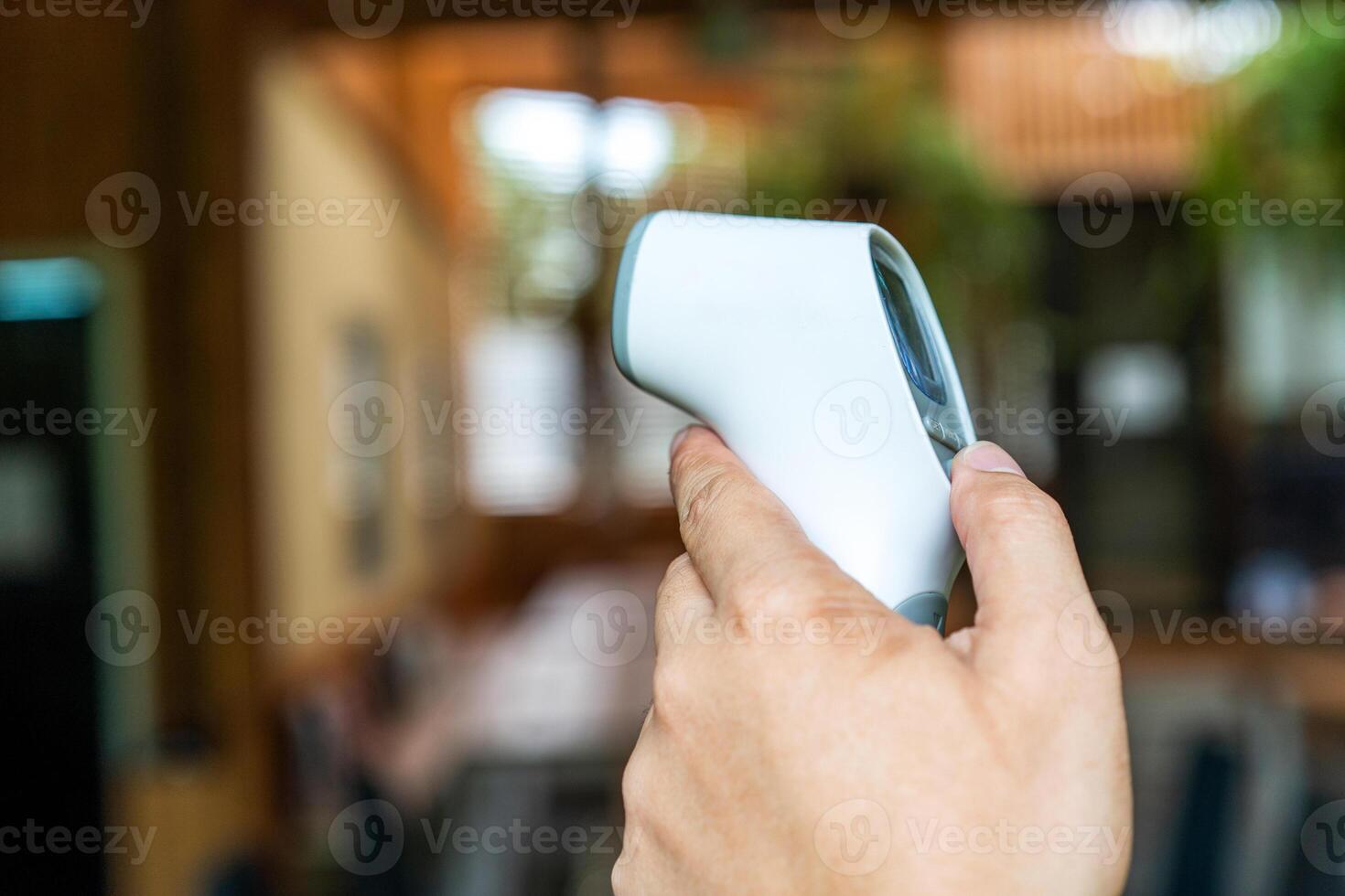 Thermometer Gun in Man's Hand. It's Digital Infrared Sight Temperature Measurement Device on wood table in outdoor field. Clipping Path. photo