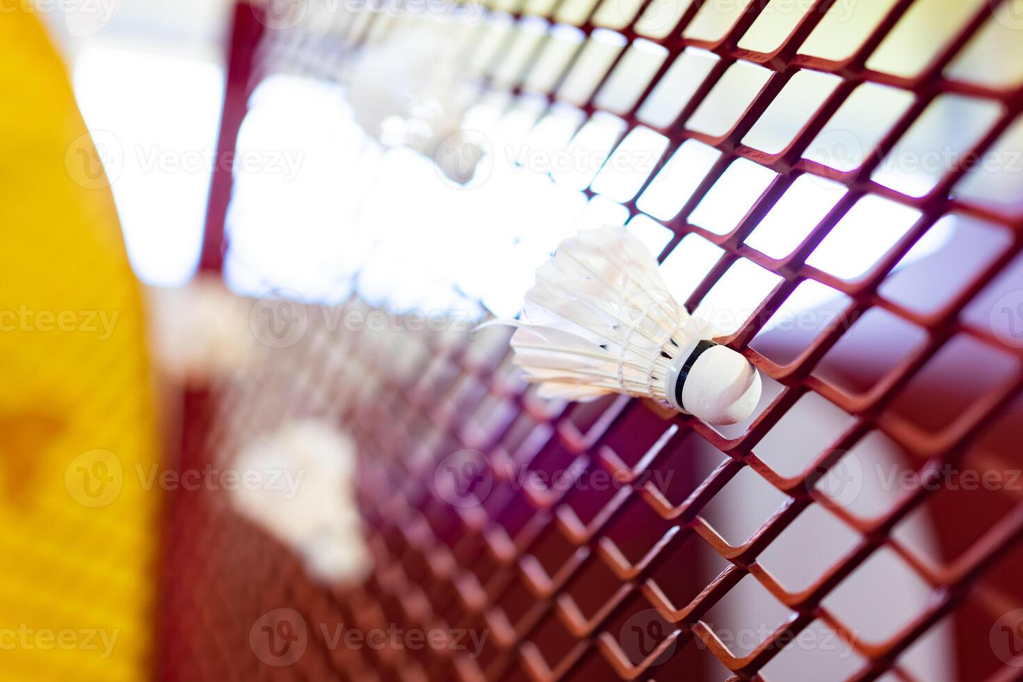 Shuttlecocks were stuck to the badminton steel grill net with a big red drawing of shuttlecock on background beside. photo