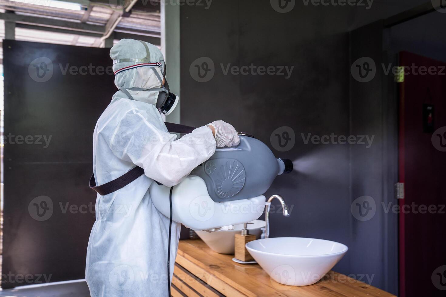 Professional technical man in prevention suit with his sterilizing machine and disinfecting water sprays in toilet or wc area field for purifying coronavirus COVID-19 photo