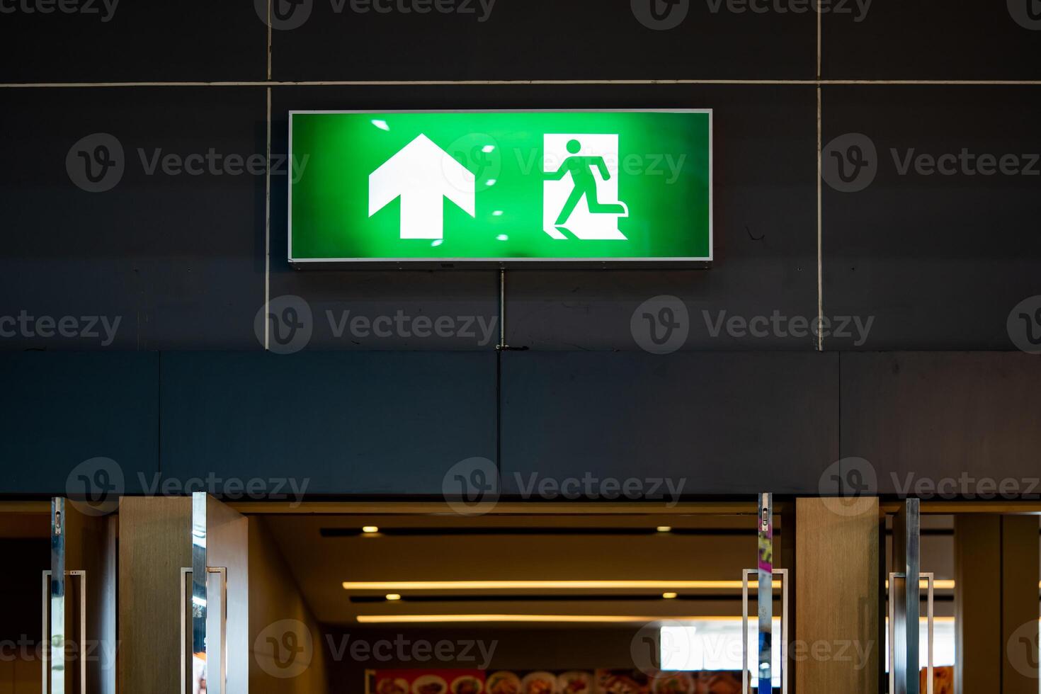 Big Emergency fire exit sign is placed on the black wall over the door of the exhibition hall. photo