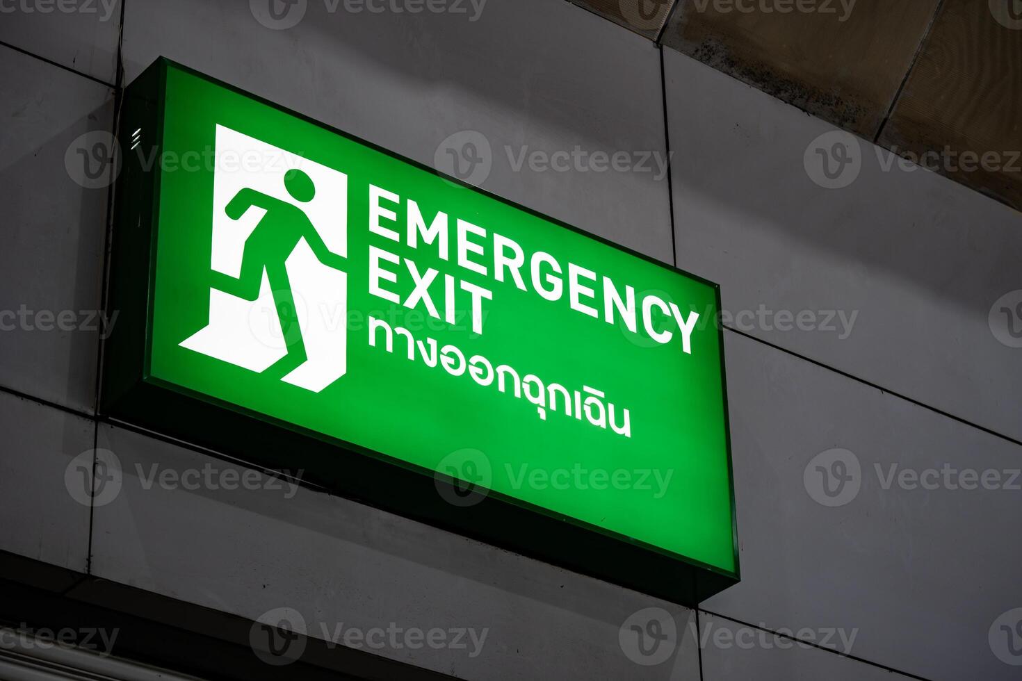Large Emergency exit sign green light box is placed on the wall of exhibition hall. Thai Letter is Thai Language on the green light box mean EXIT. photo