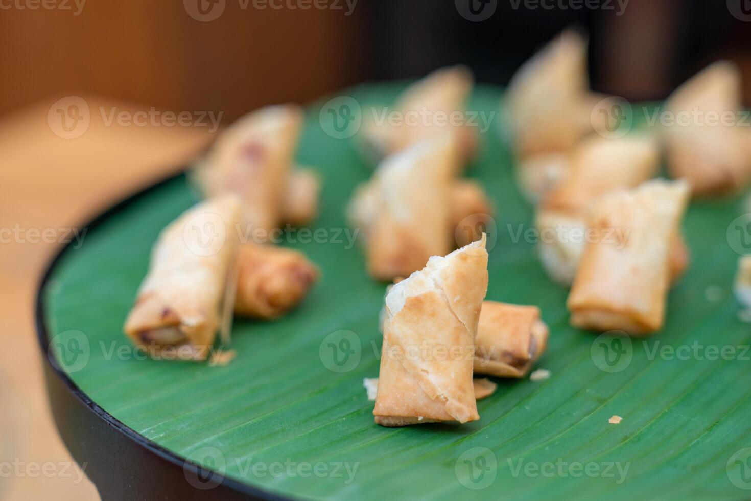 Deep fried spring roll vegetable and vermicelli on circle black plate with banana leaf at an outdoor wood table. photo