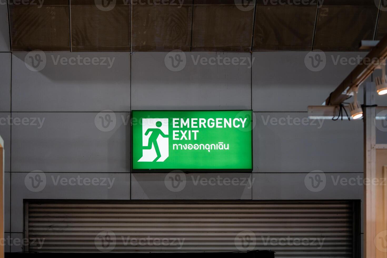 Large Emergency exit sign green light box is placed on the wall of exhibition hall. Thai Letter is Thai Language on the green light box mean EXIT. photo