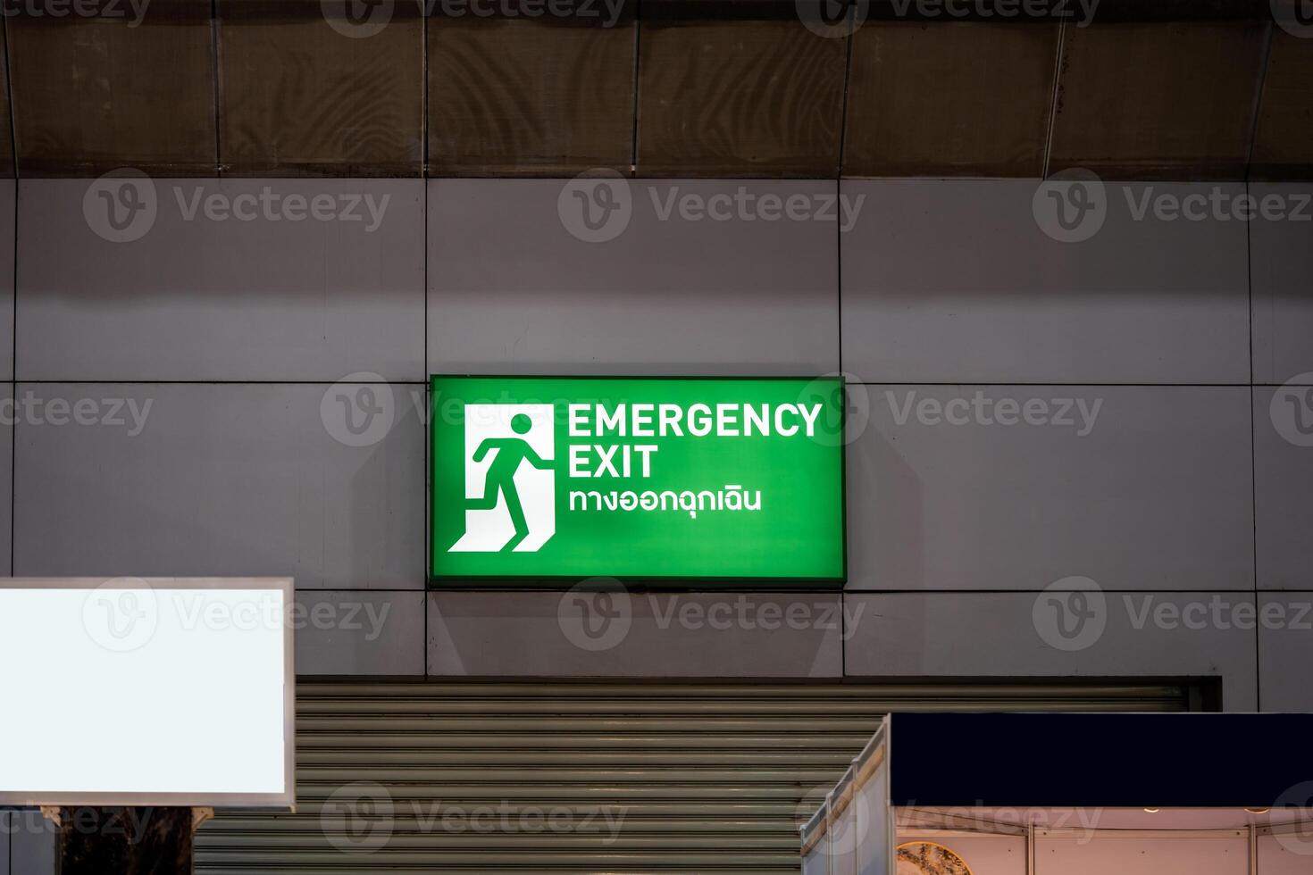 Large Emergency exit sign green light box is placed on the wall of exhibition hall. Thai Letter is Thai Language on the green light box mean EXIT. photo