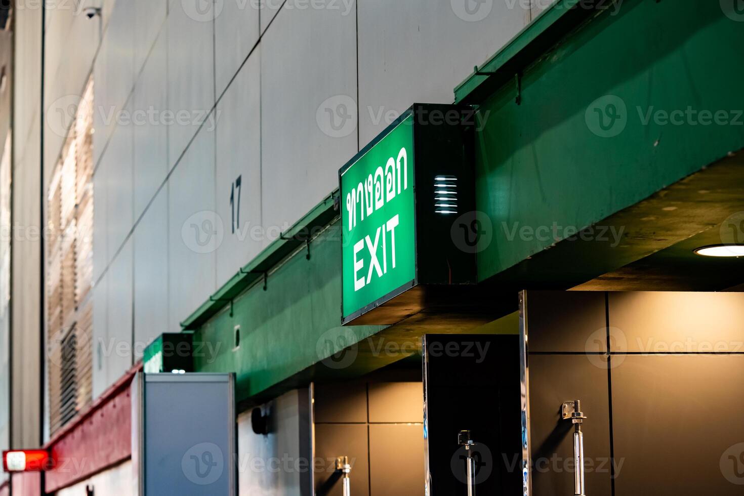 Large Emergency exit sign green light box is placed on the wall of exhibition hall. Thai Letter is Thai Language on the green light box mean EXIT. photo