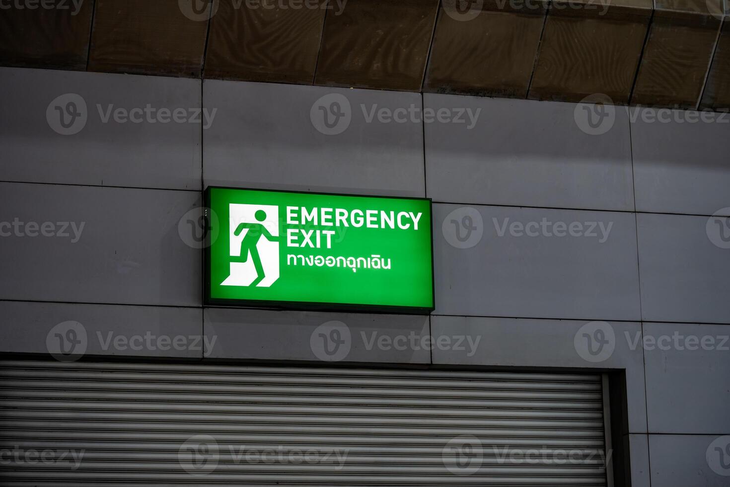 Large Emergency exit sign green light box is placed on the wall of exhibition hall. Thai Letter is Thai Language on the green light box mean EXIT. photo
