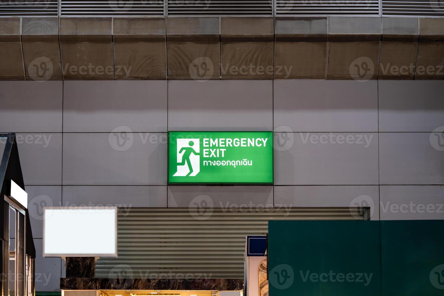 Large Emergency exit sign green light box is placed on the wall of exhibition hall. Thai Letter is Thai Language on the green light box mean EXIT. photo