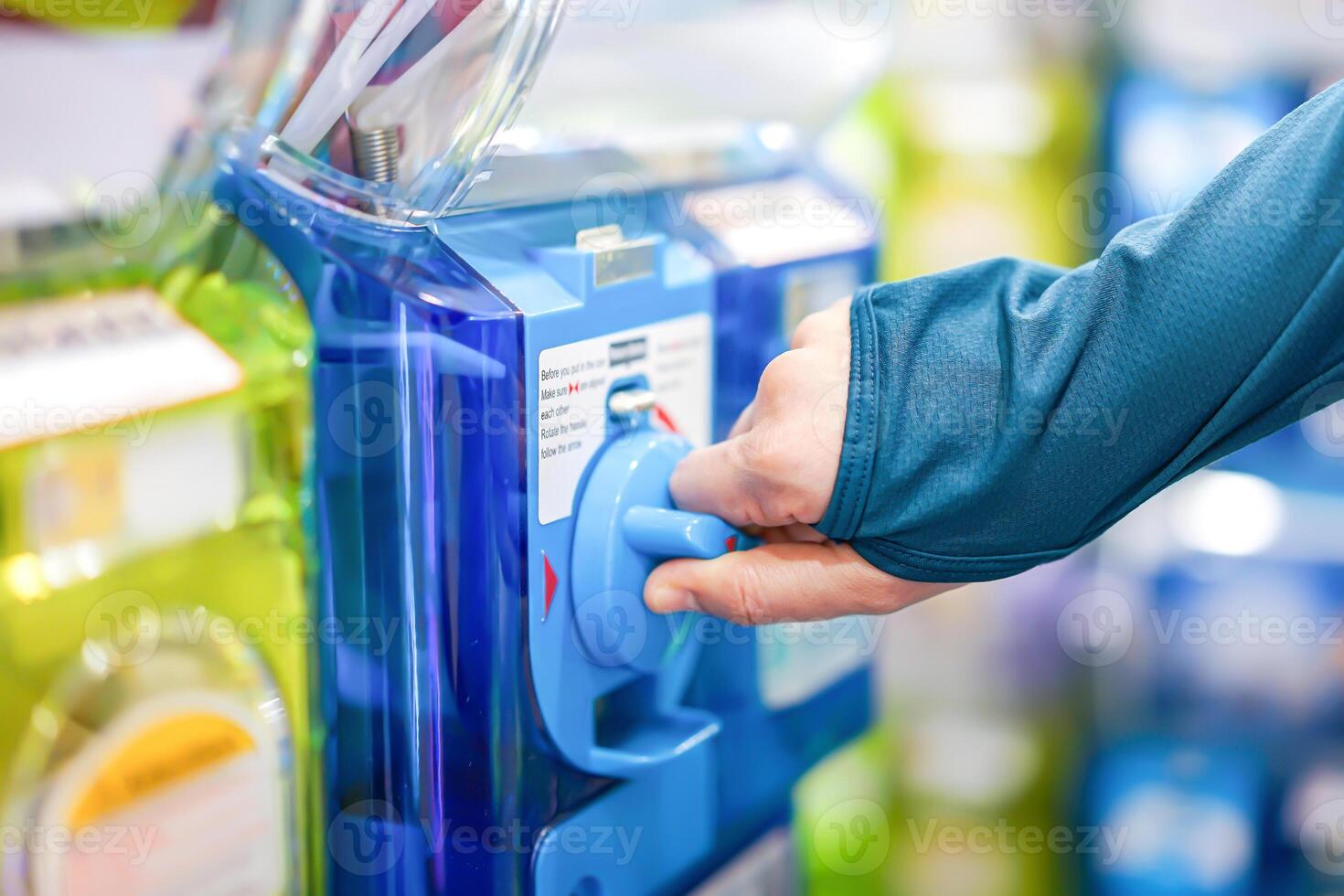 A human hand in a turquoise sweater is twisting a blue gashapon machine to release a figure. In Japan, it is considered as one of the most well liked risks. photo